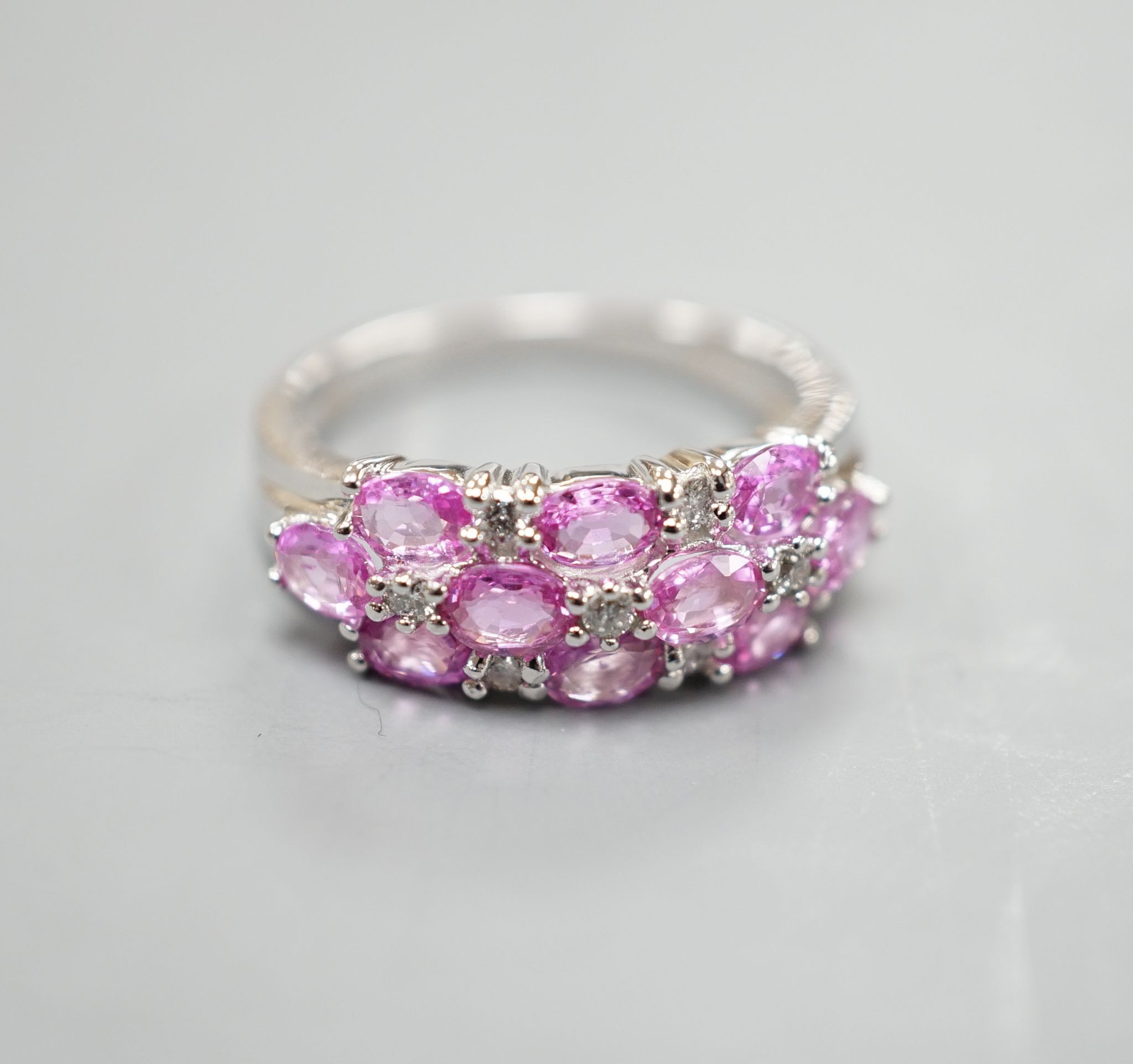 A modern 14k white metal, pink sapphire and diamond cluster set half hoop dress ring, size O, gross weight 4.6 grams.